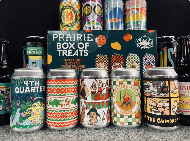 A box of prairie box of treats is surrounded by cans and bottles of beer.