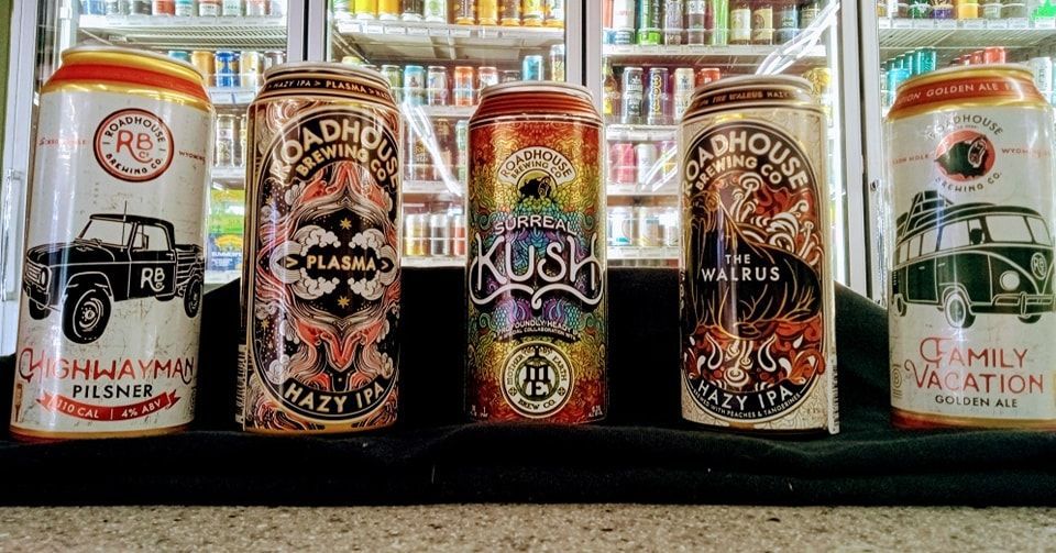 Four cans of beer are sitting on a table in front of a refrigerator.