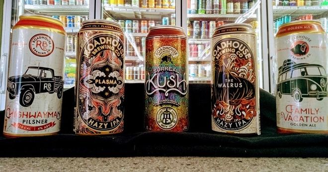 Four cans of beer are sitting on a table in front of a refrigerator.
