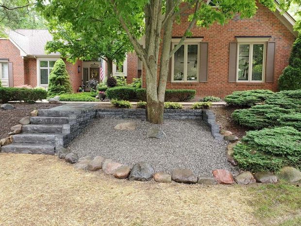 Brick house front yard with stone steps, gravel bed, and a tree in the center