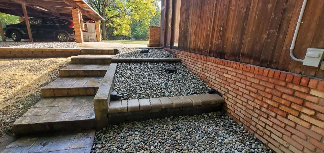 Raised gravel pathway with stone steps beside a brick wall and wooden fence in a yard