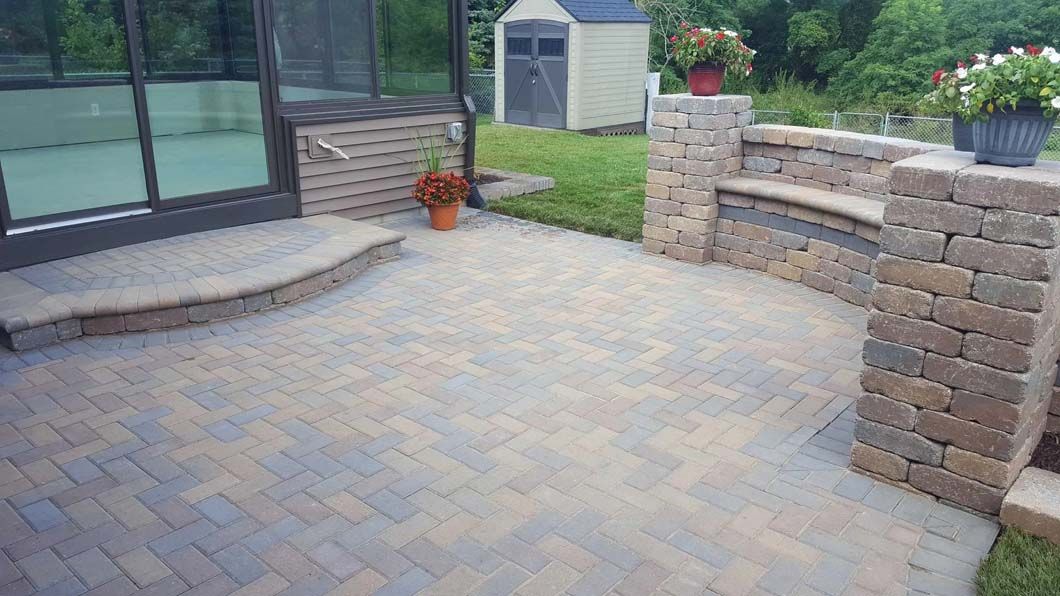 Brick patio beside house with curved steps, low retaining wall, potted plants, and a small shed in the yard