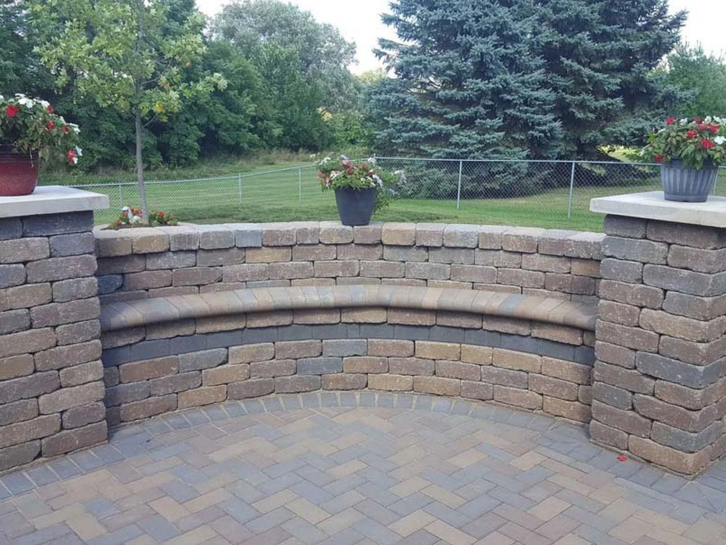 Curved stone patio wall with potted flowers in a landscaped backyard garden