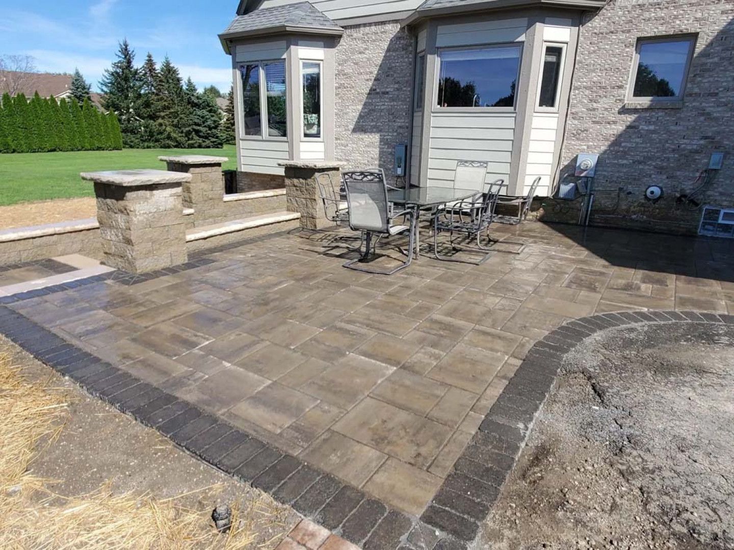 Stone patio with outdoor table and chairs beside a house, bordered by gravel and a low wall.
