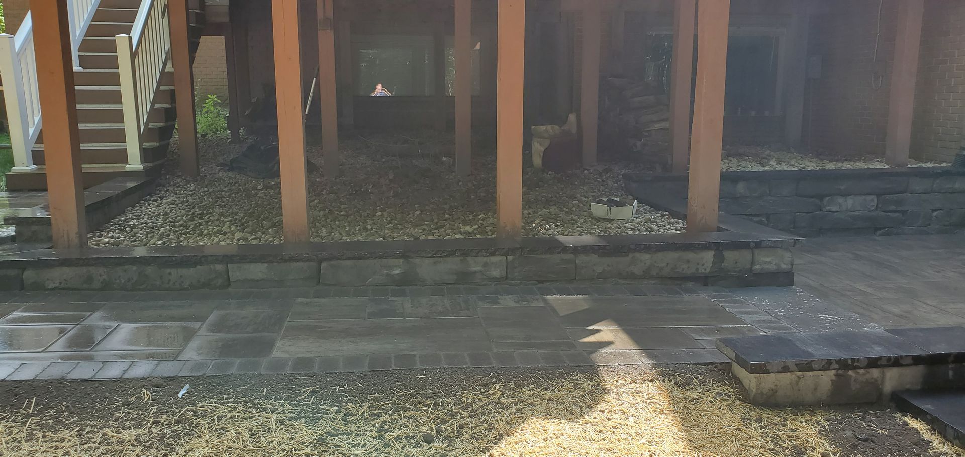 Weathered wooden deck supports over a gravel and stone path in bright sunlight.