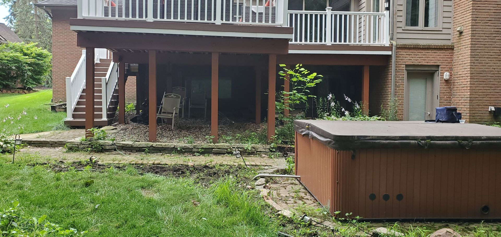 Backyard deck and patio with a hot tub, grass, and a brick house in the background