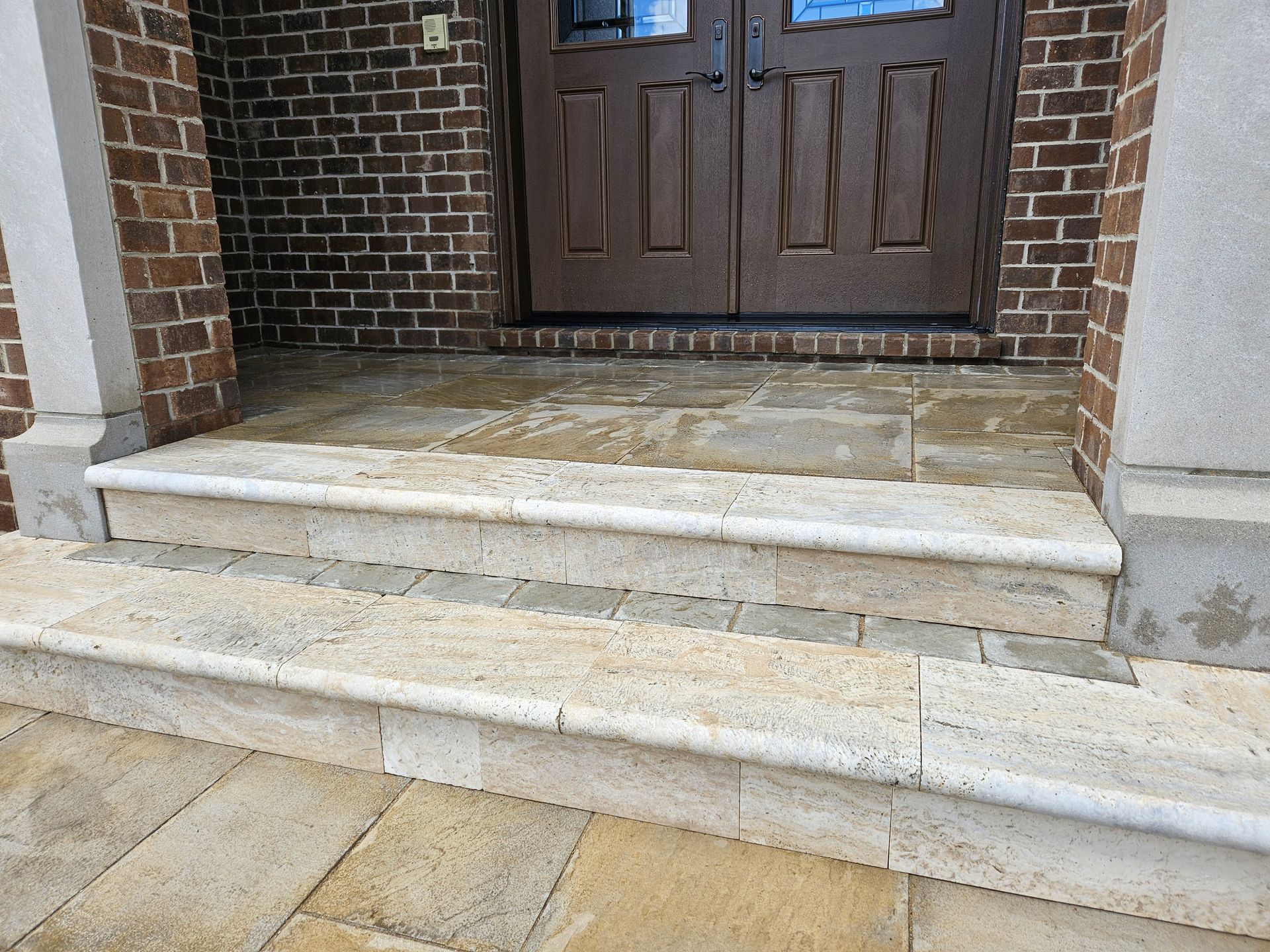 Stone front steps leading to a dark wooden double door in a brick entryway