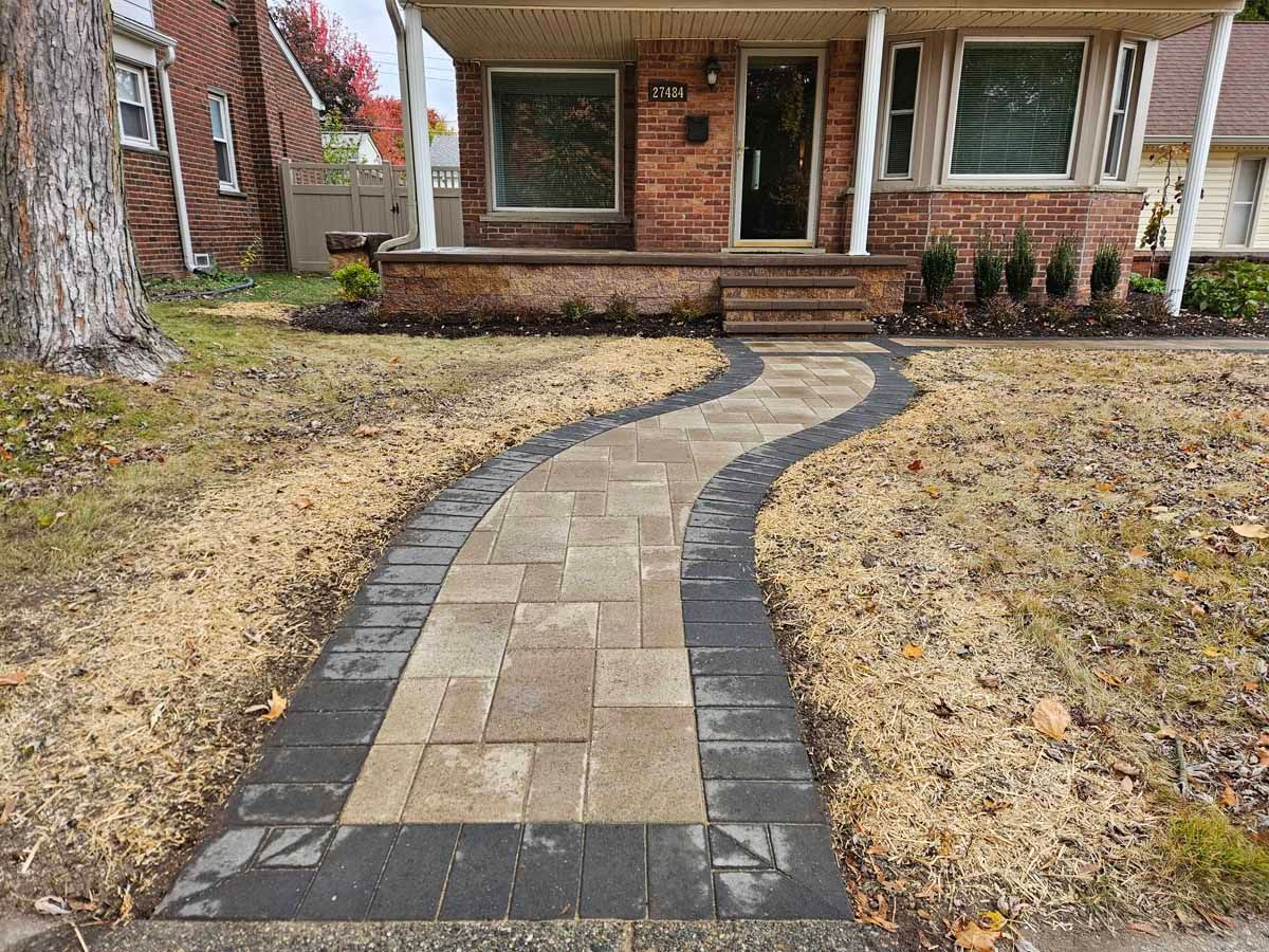 Curved stone walkway leading to a brick house porch, bordered by winter-dormant grass and dark edging
