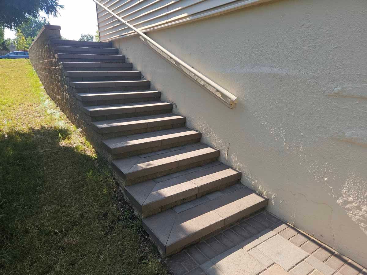 Outdoor concrete stairway beside a beige wall and grassy slope, lit by sunlight.