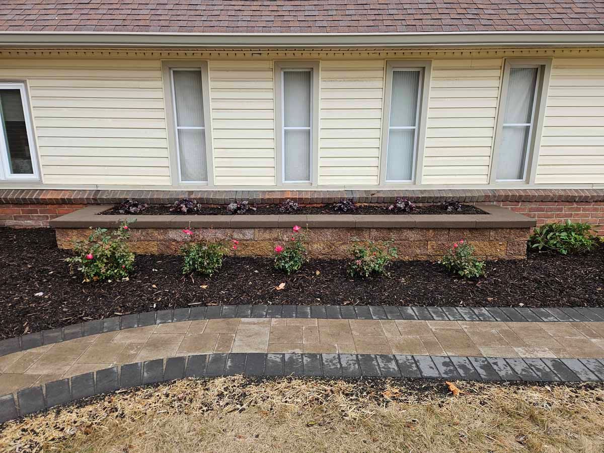 Landscaped front of a house with brick edging, dark mulch beds, and small shrubs beneath windows.