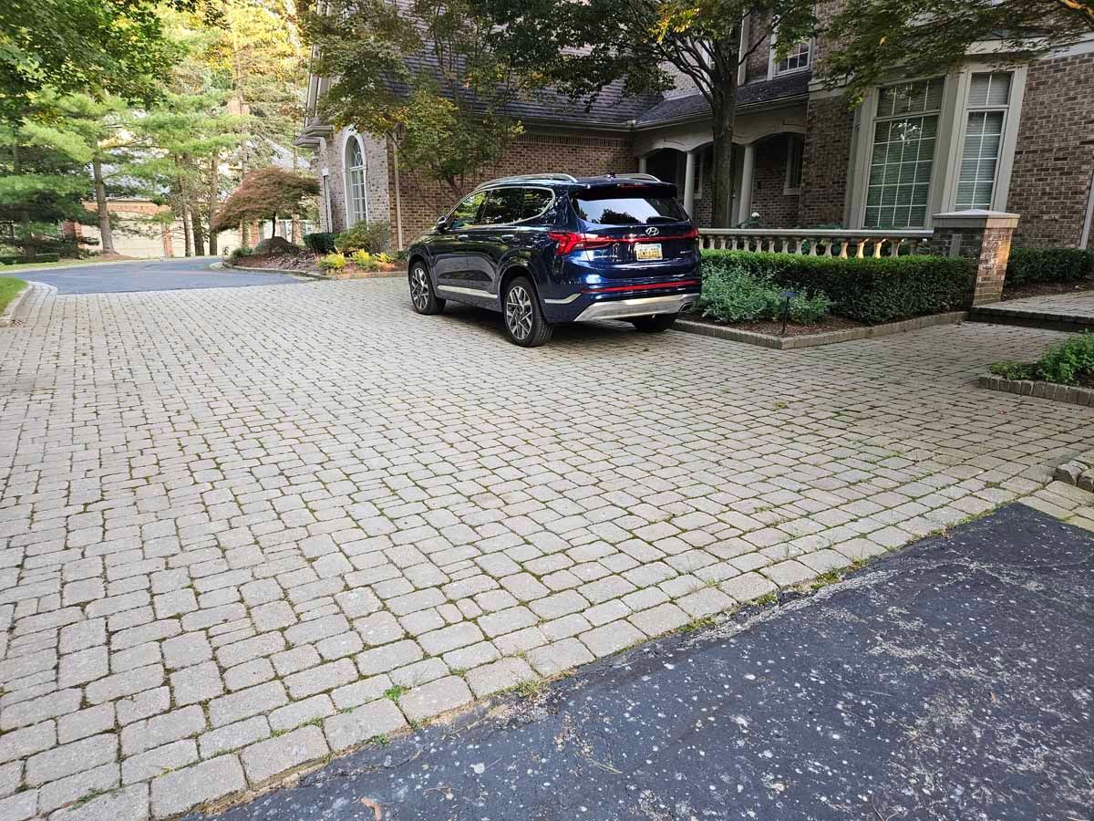 Black SUV parked on a cobblestone driveway beside a brick building with trees and greenery.