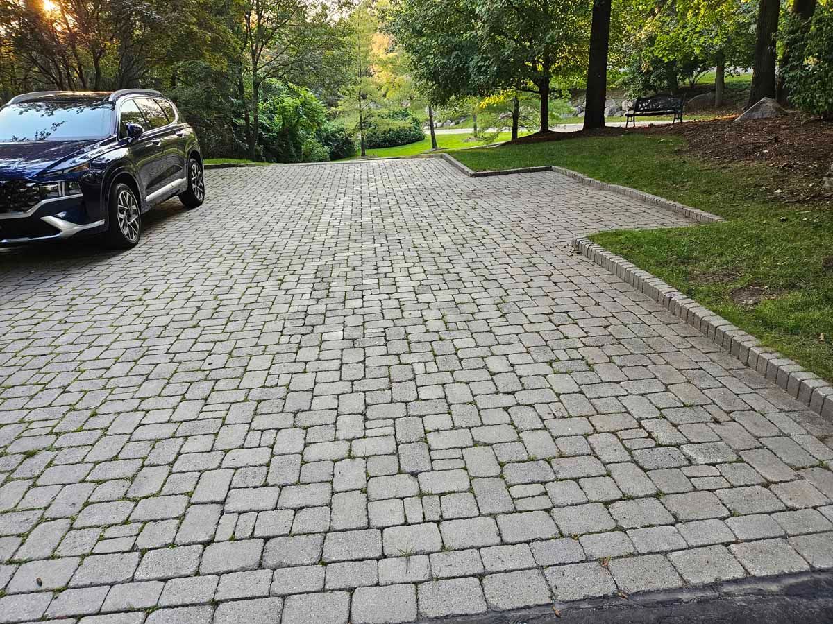 Black SUV parked beside a cobblestone driveway in a wooded park-like area.