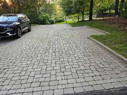 Black SUV parked beside a cobblestone driveway in a wooded park-like area.