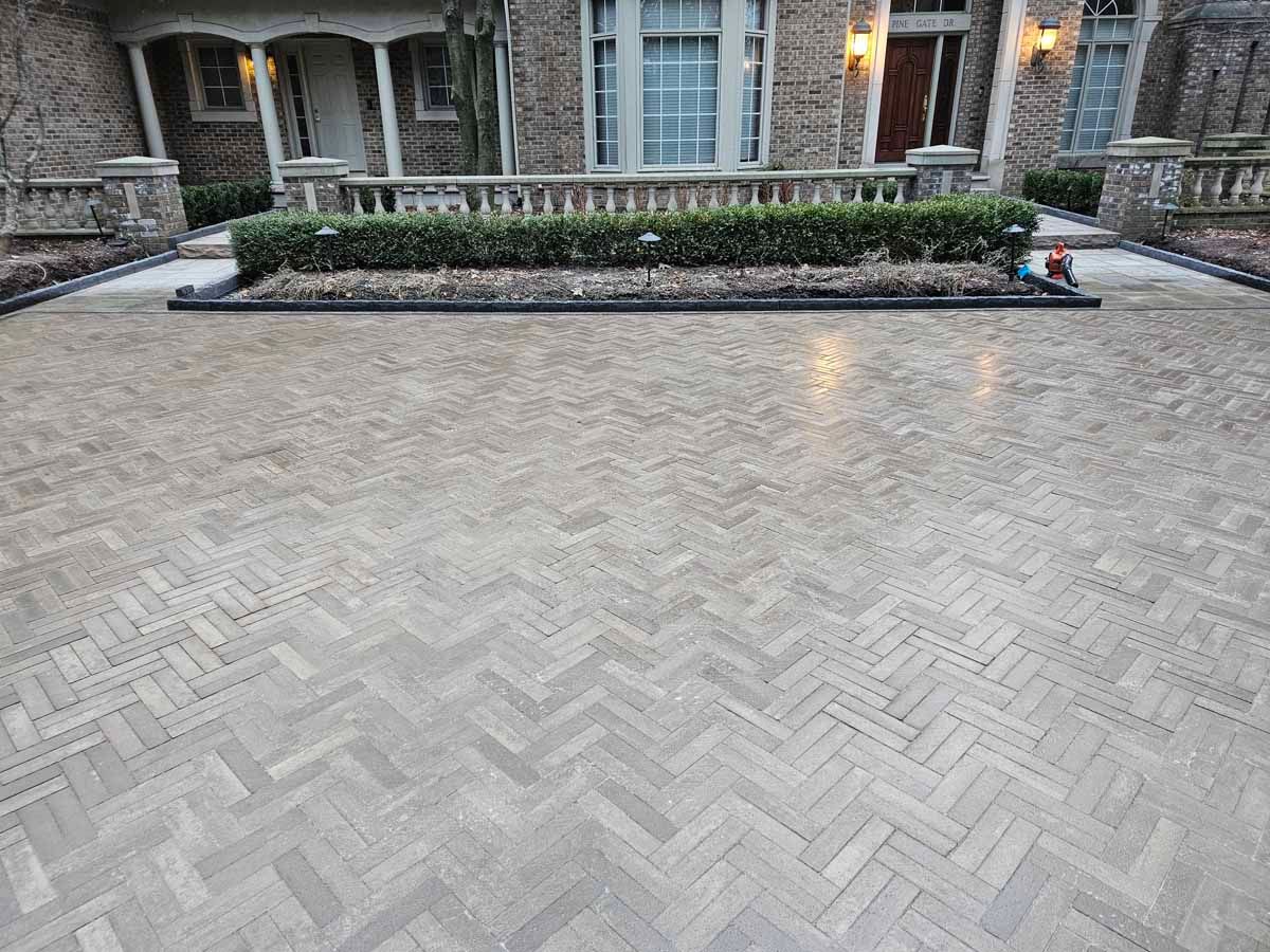 Herringbone brick courtyard with a low stone planter in front of an apartment building entrance.