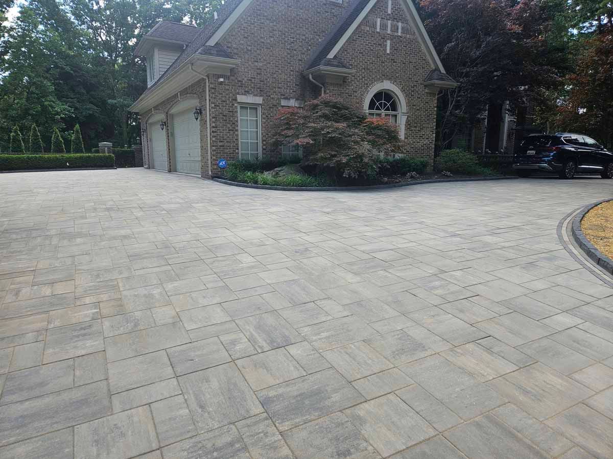 Stone-paved driveway beside a brick house with garage and landscaped front yard.