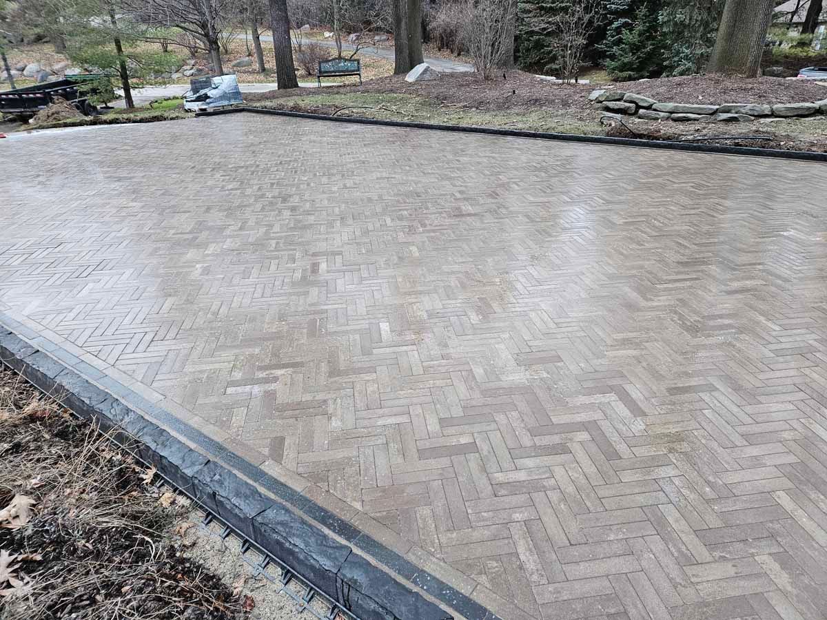 Empty brick-paved courtyard bordered by low stone edges and trees in the background