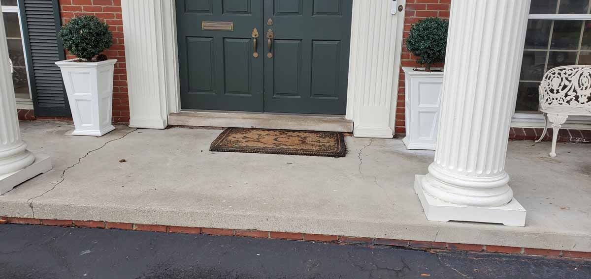 Front porch with dark double doors, white columns, two potted plants, and a doormat on the concrete steps