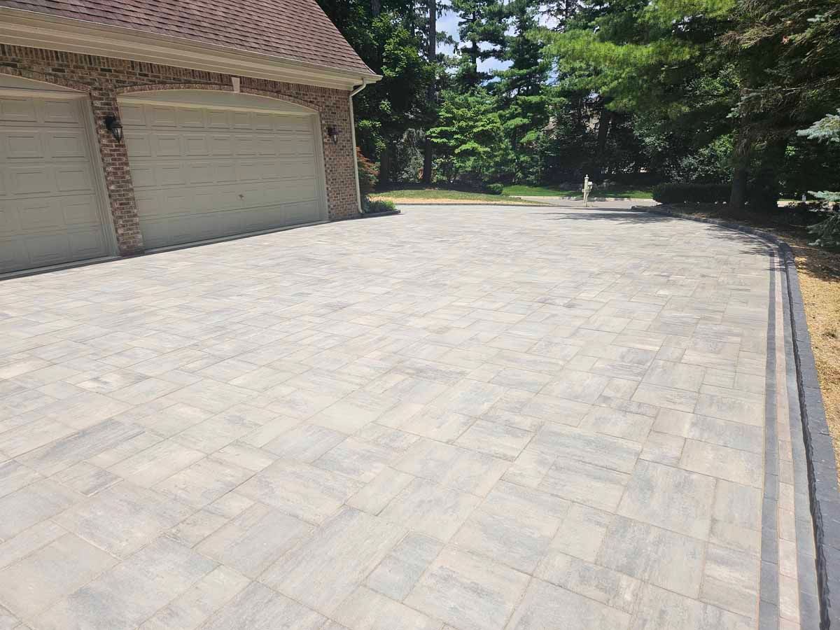 Large paved driveway beside a garage and trees on a sunny day