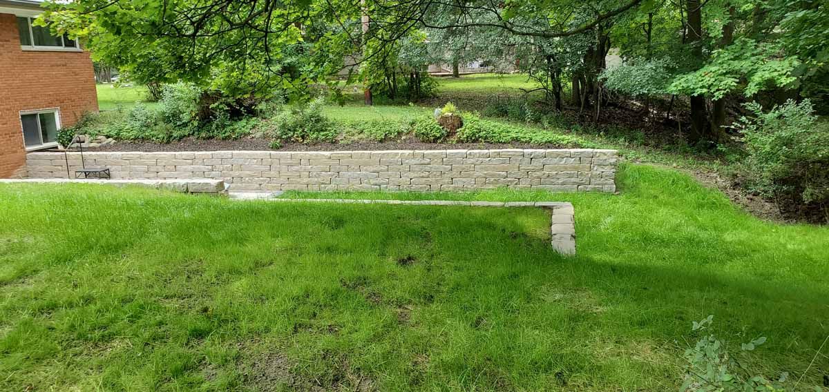 Green yard with a low stone retaining wall and trees in the background