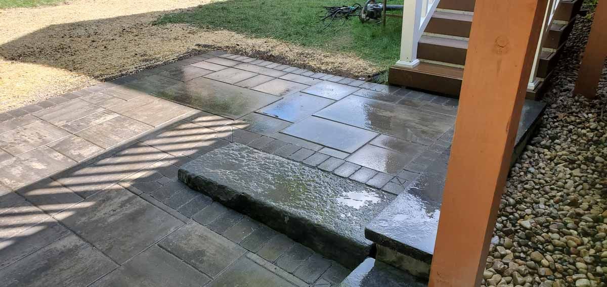 Outdoor patio with uneven steps and wet stone paving beside a brick building