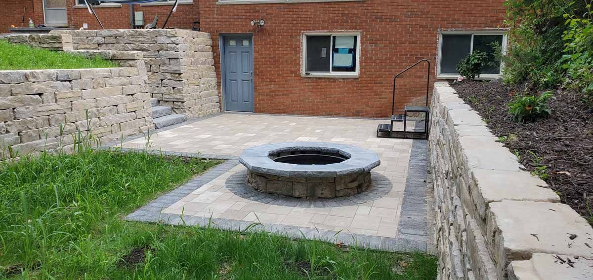 Brick courtyard with a circular stone fire pit and low retaining walls by a building