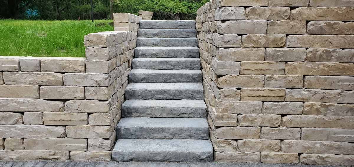 Stone steps between tan retaining walls with green grass above