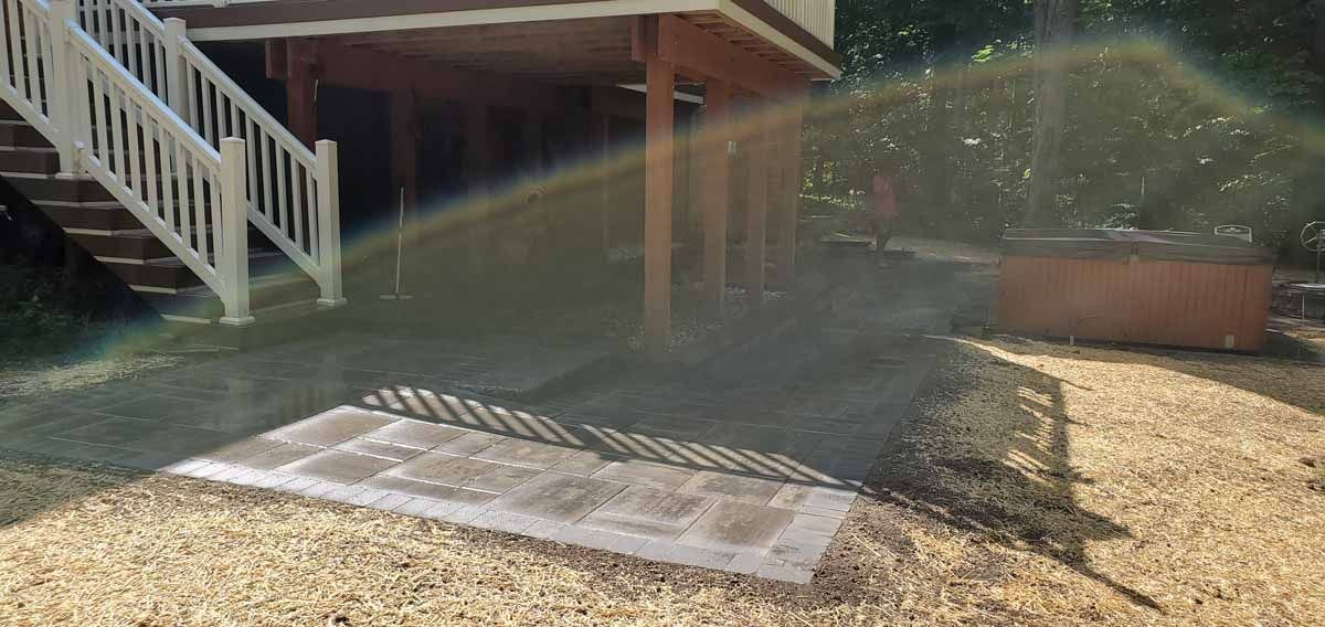 Metal ramp on gravel beside a brick building, with sunbeam and stairs in the background.
