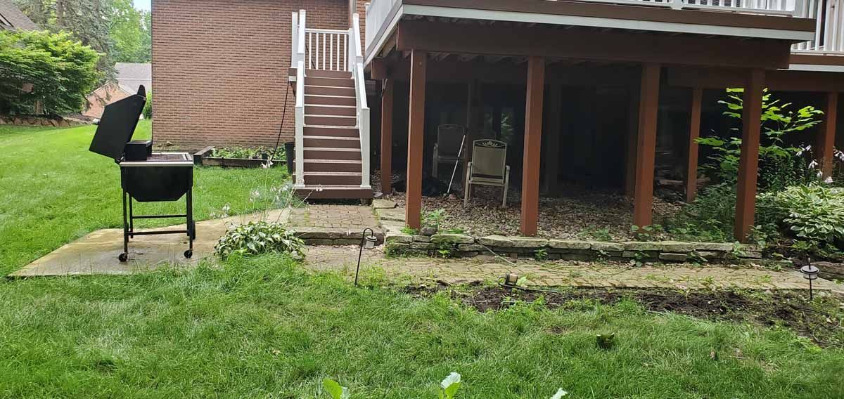 Backyard with a black grill on grass beside a house and wooden stairs leading to a covered patio