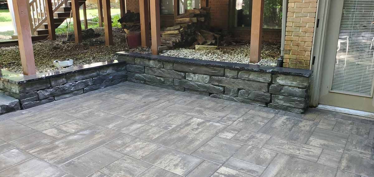 Stone patio with raised retaining wall and wooden deck posts beside a glass door