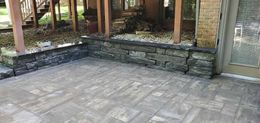 Stone patio beside a raised garden bed and wooden posts, with a glass door on the right