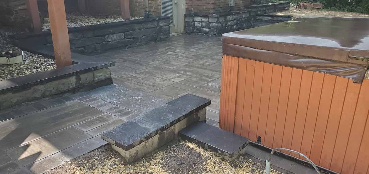 Wet stone patio and wooden hot tub beside a garden walkway after rain.