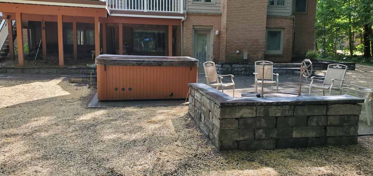 Backyard patio with a hot tub and stone fire pit in front of a wooden house