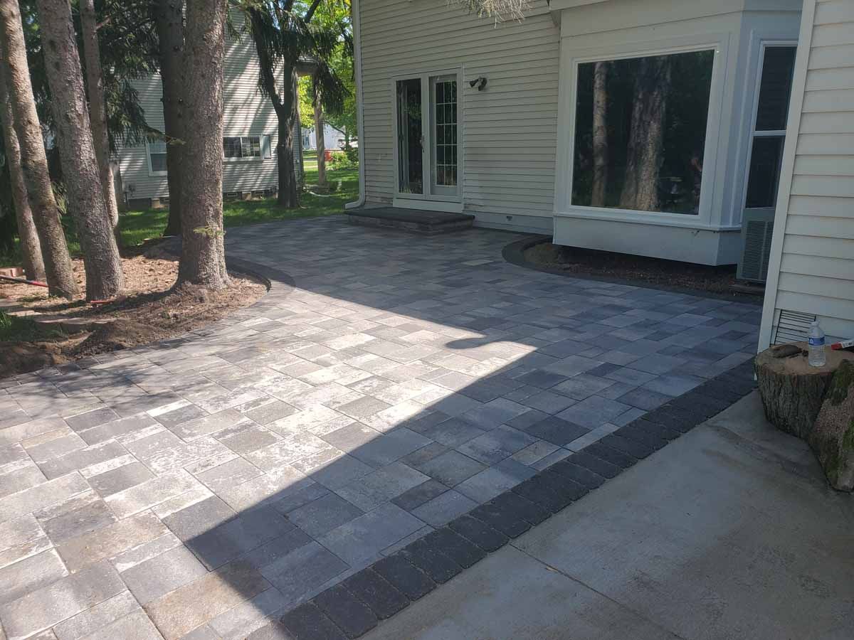 Stone patio with dark border pavers beside a house and trees in the yard