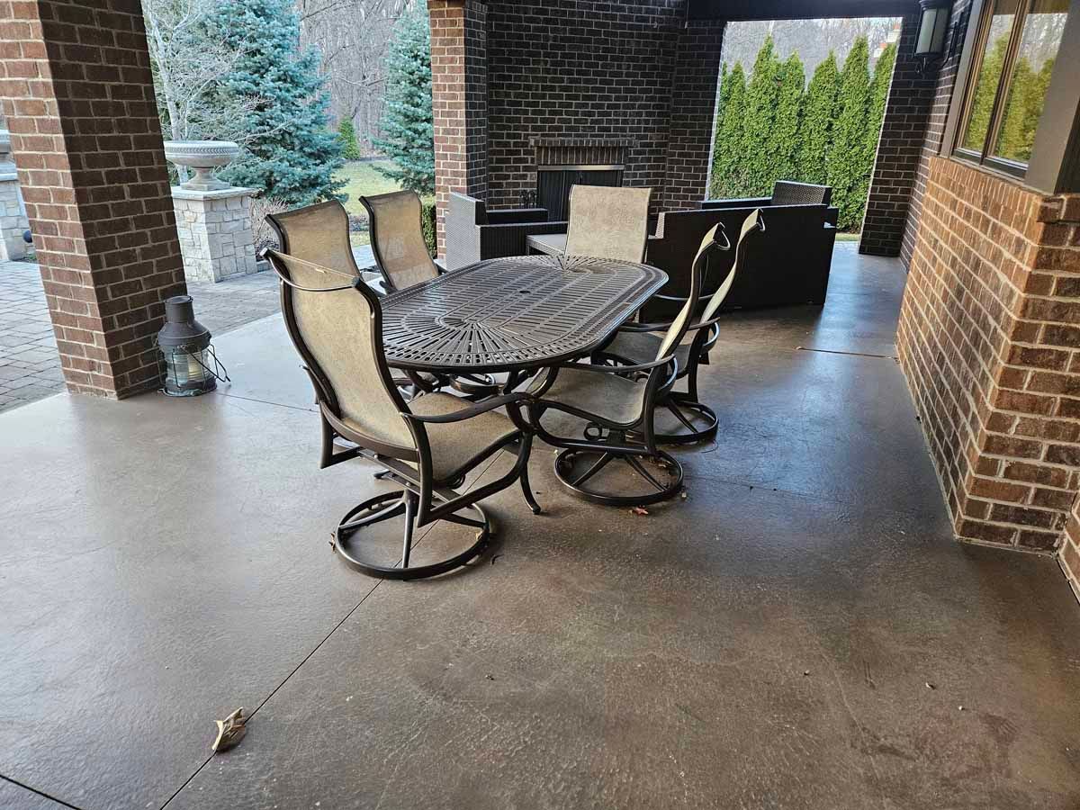 Covered patio with glass-top table, four chairs, and brick columns overlooking a yard
