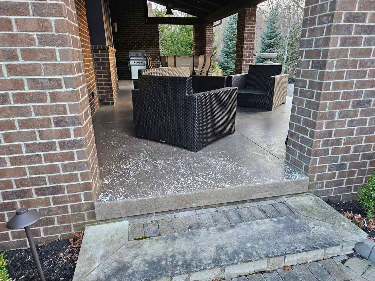 Covered brick patio with wicker chairs and a concrete step at the entrance