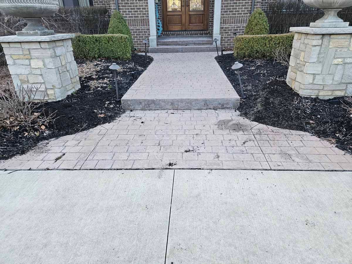 Stone walkway leading to a front door, bordered by low stone pillars and landscaping.