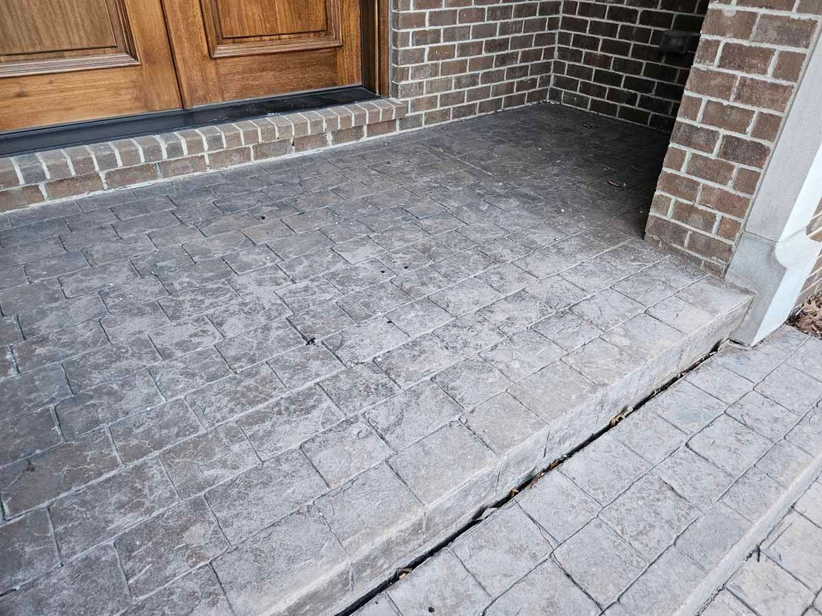 Stone front porch with brick walls and a wooden door, showing a raised threshold step.
