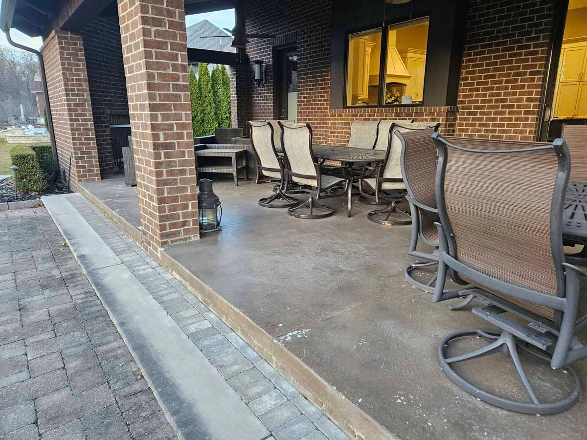Covered brick patio with metal chairs and table beside a house at dusk