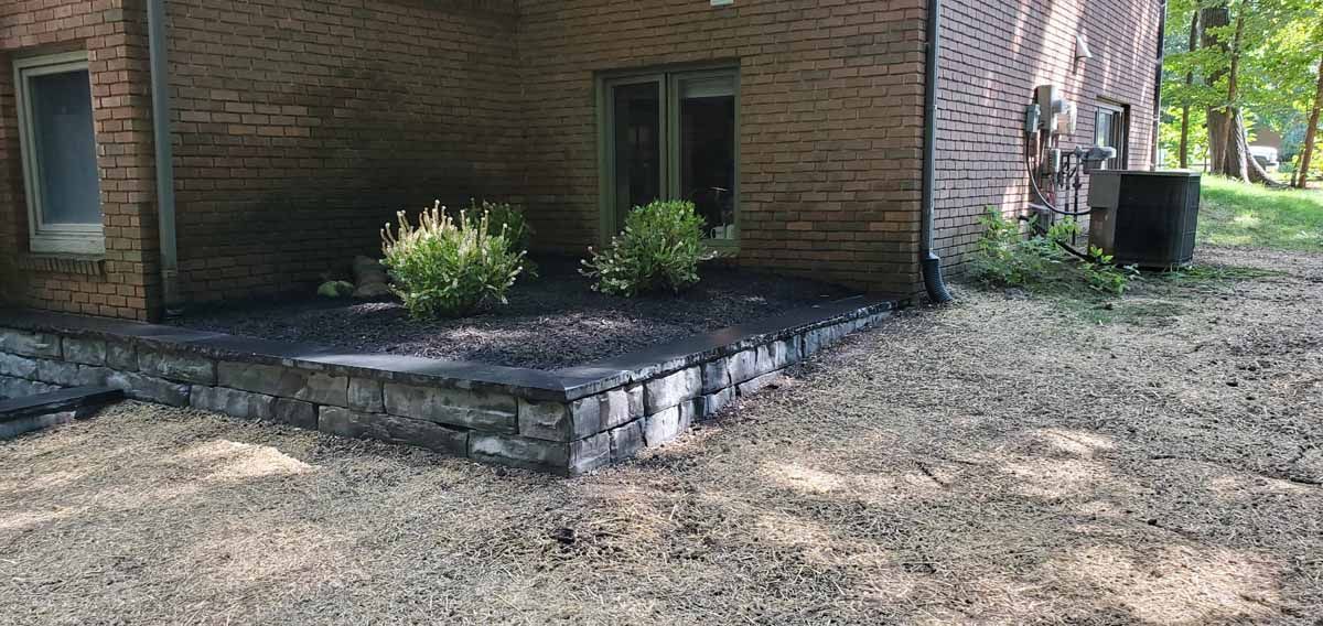 Brick house side yard with a small raised stone patio and sparse landscaping