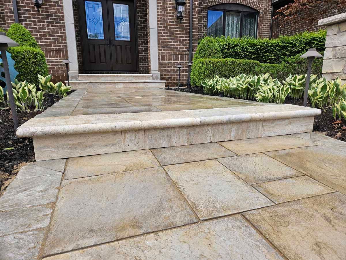 Stone front steps leading to a brick house entrance with trimmed green hedges and a paved walkway