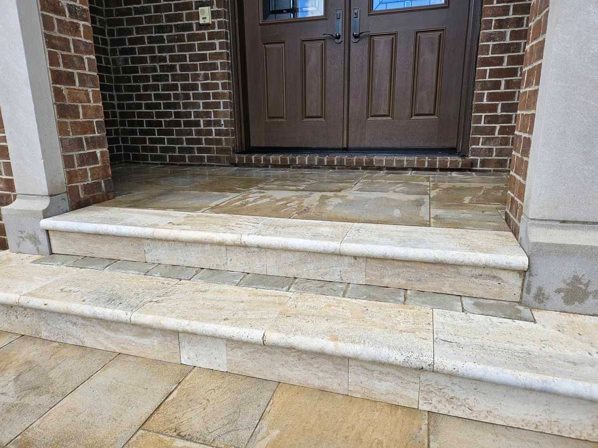 Front steps of a brick house with a brown double door and light stone stairs