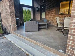 Brick patio porch with wicker loveseat, chairs, and a narrow walkway beside a house entrance