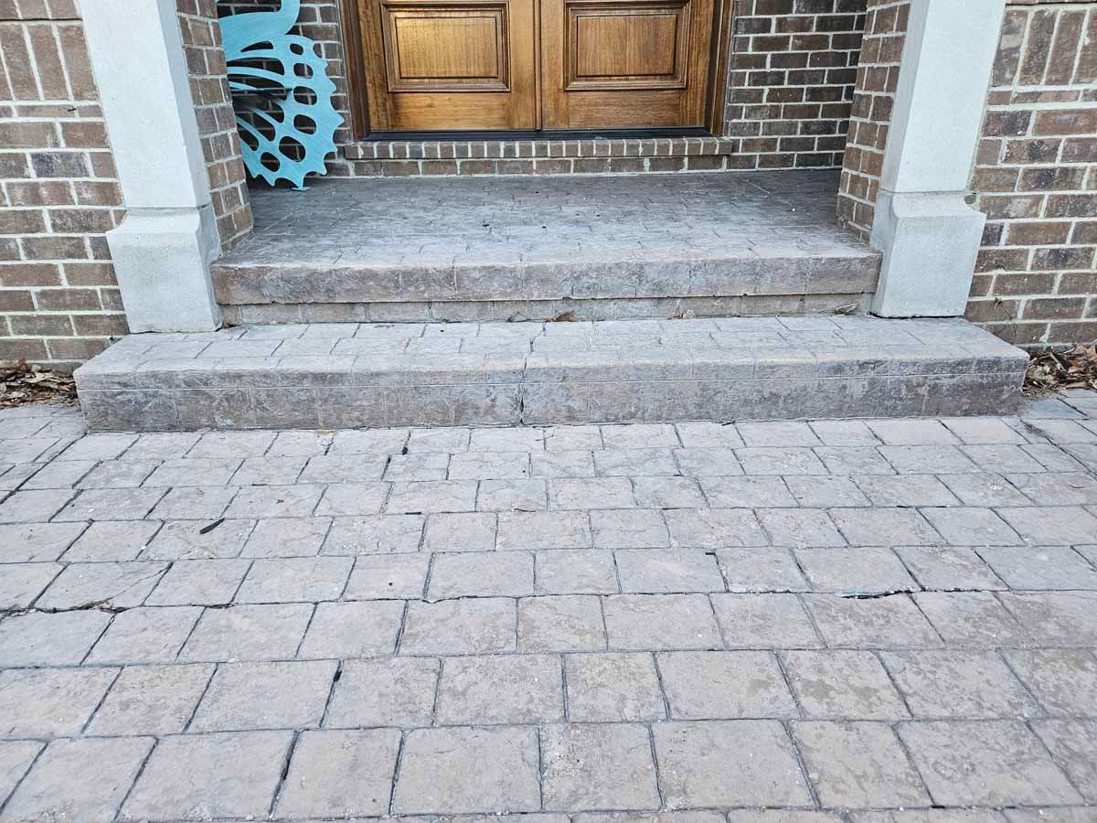 Stone steps leading to a wooden front door with brick columns and a paved walkway