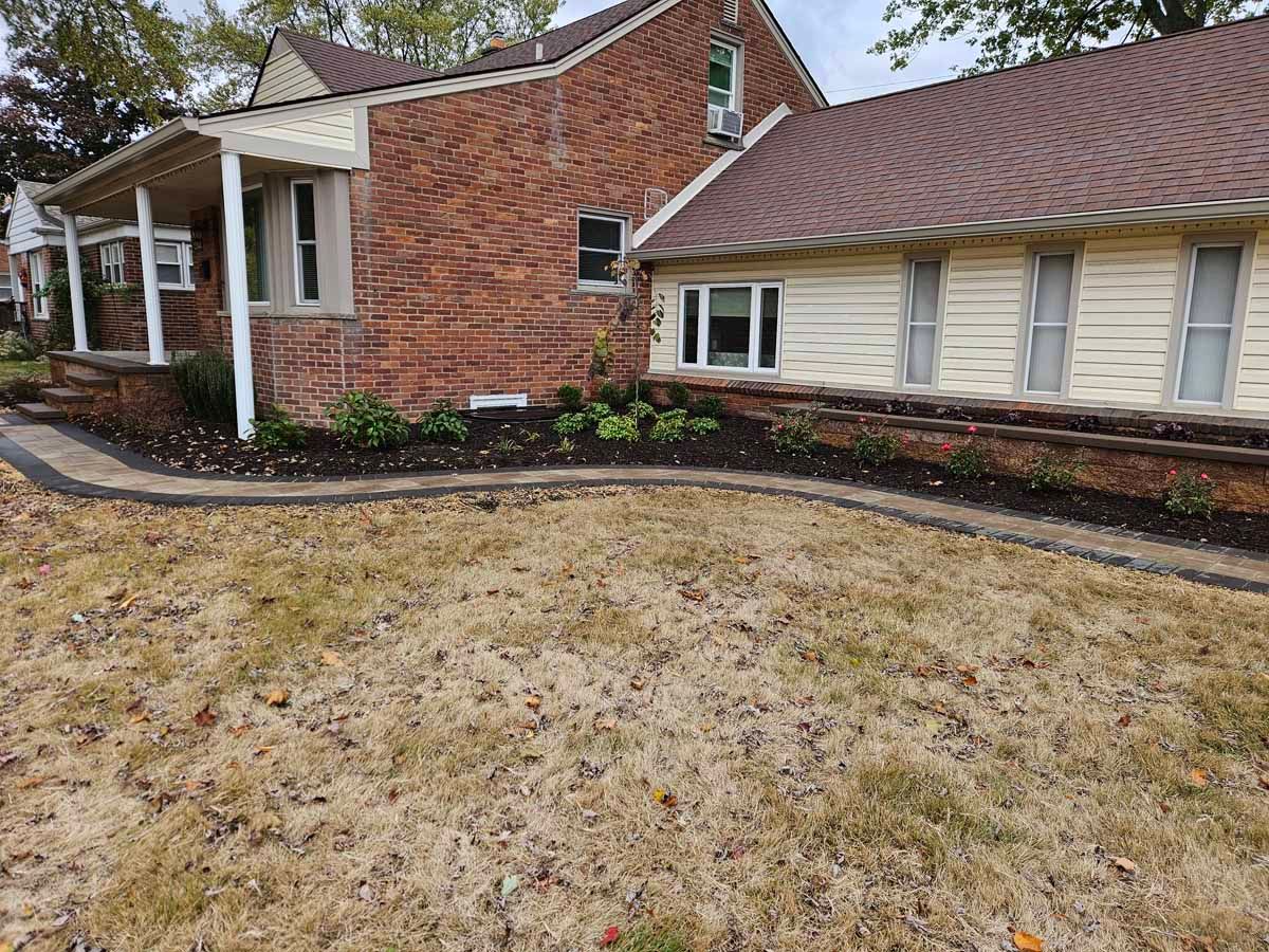 Brick house and front yard with dry grass, white-trimmed windows, and a curved garden bed