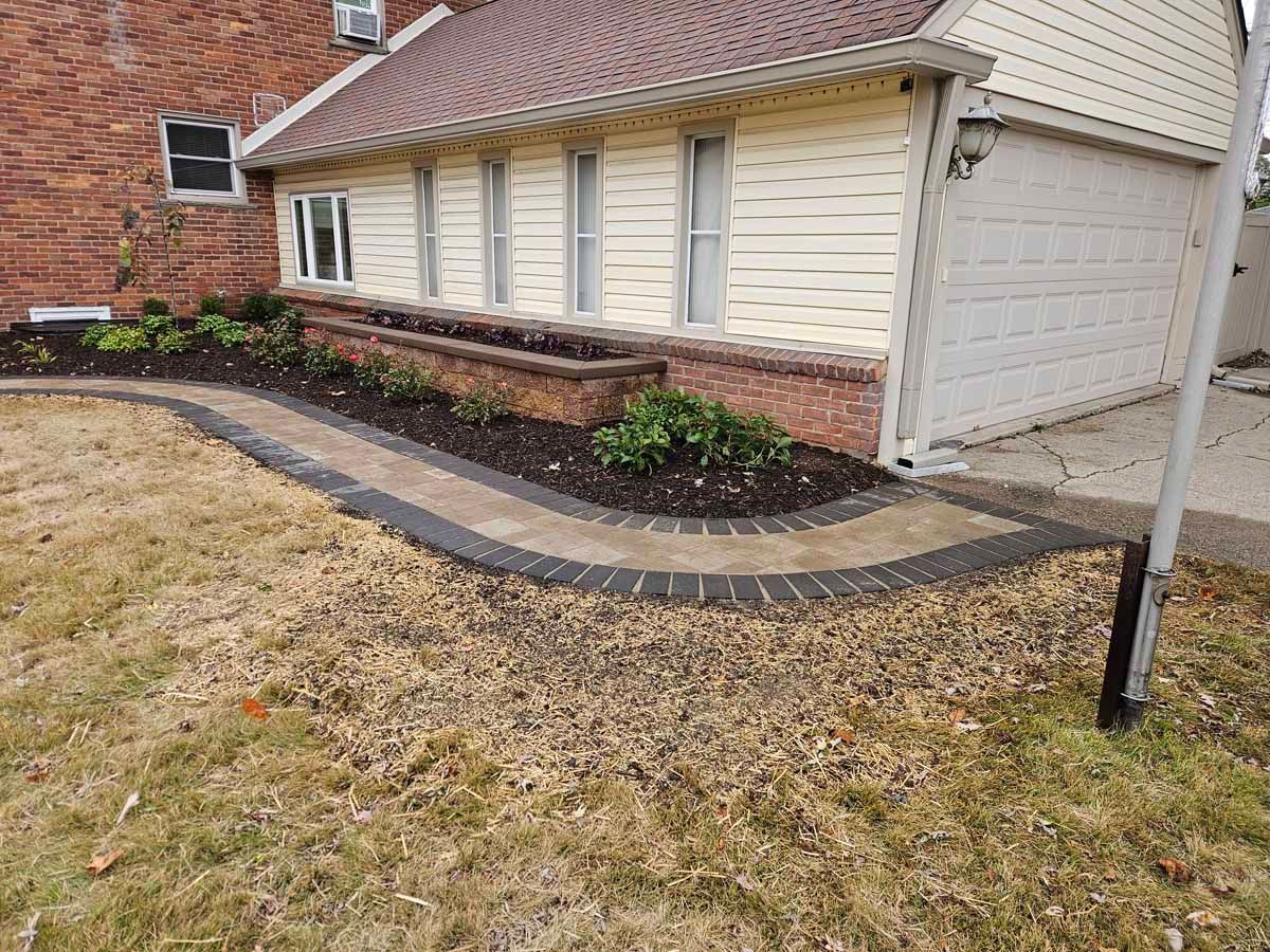 Front yard landscaping with curved black edging along a brick house and garage.