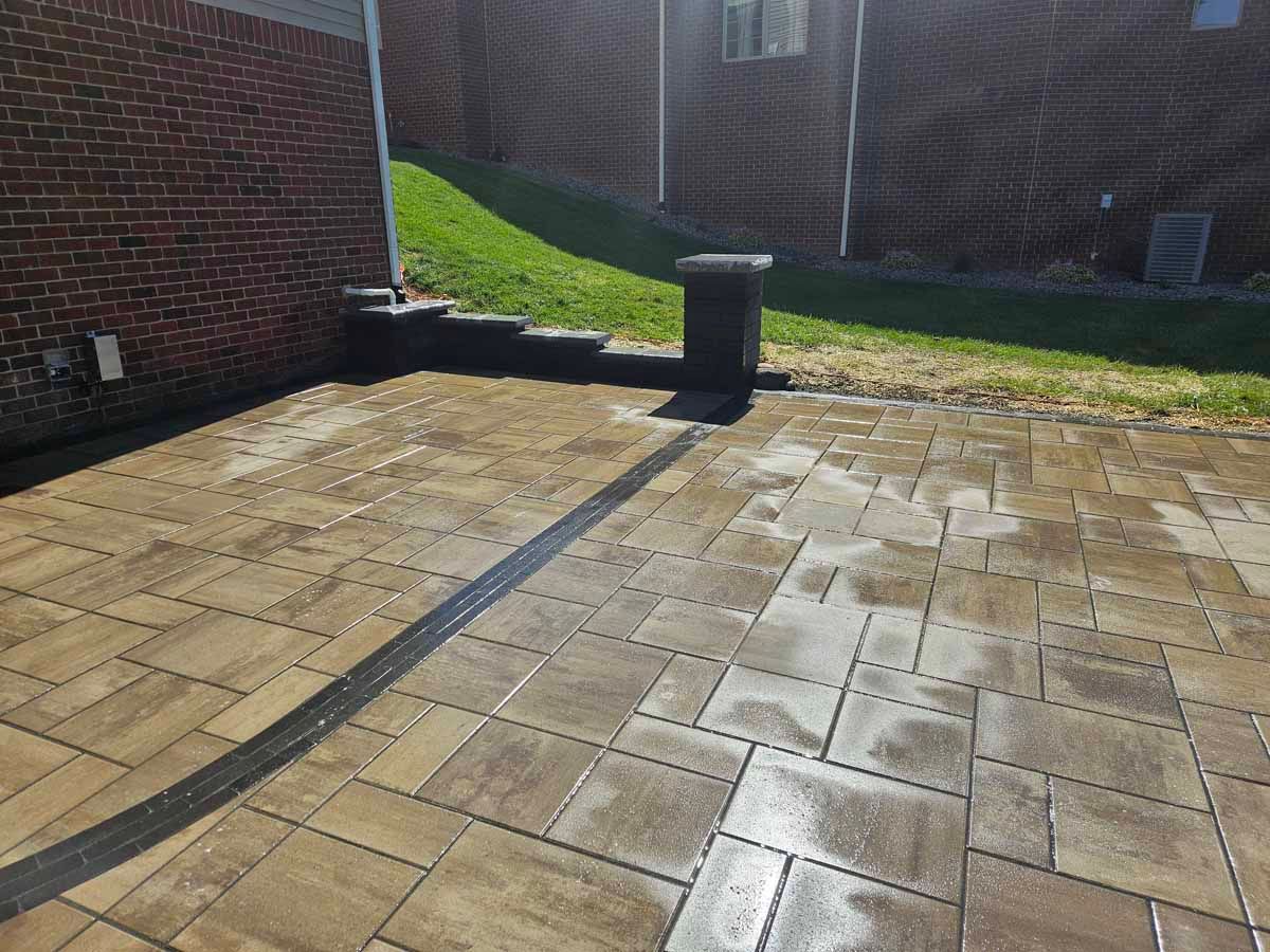 Sunlit brick patio beside a brick wall with a short black post and wet patches on the paving