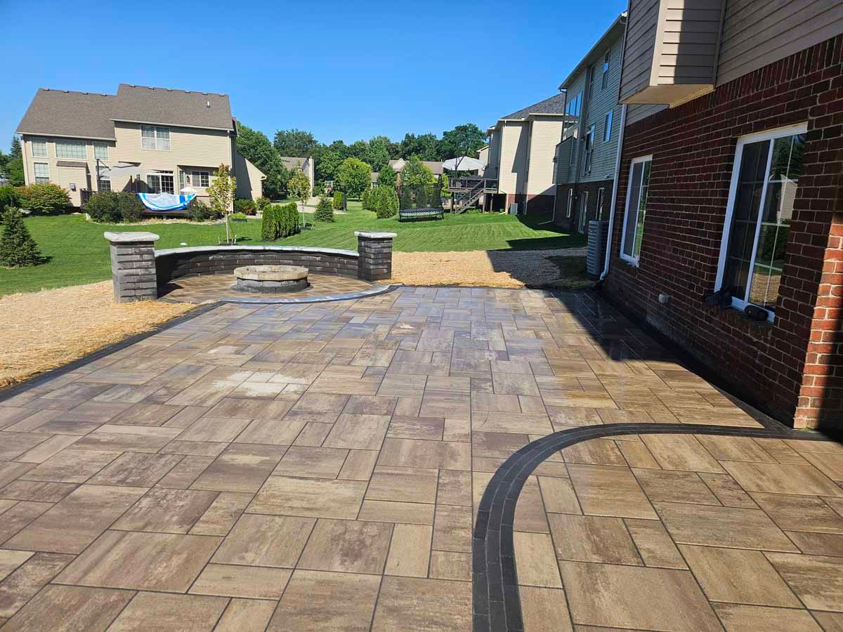 Brick patio in a suburban neighborhood, with stone planters and houses in the background.