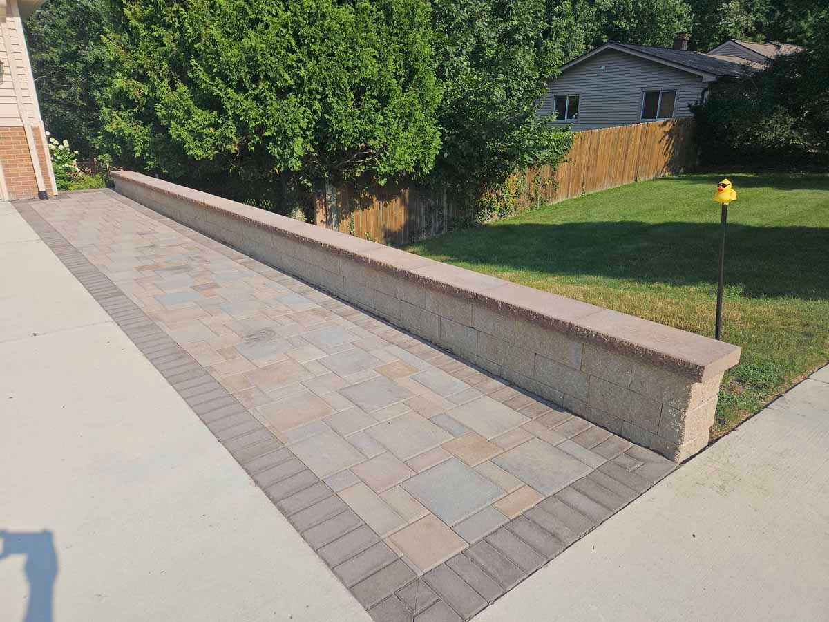 Concrete walkway with a low retaining wall beside a grassy yard and trees.