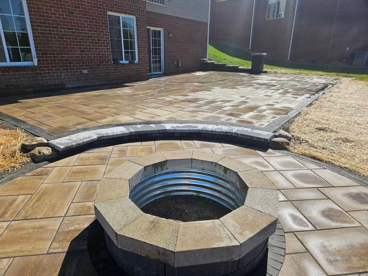 Brick courtyard with open circular drain or manhole and a hose lying across the pavement