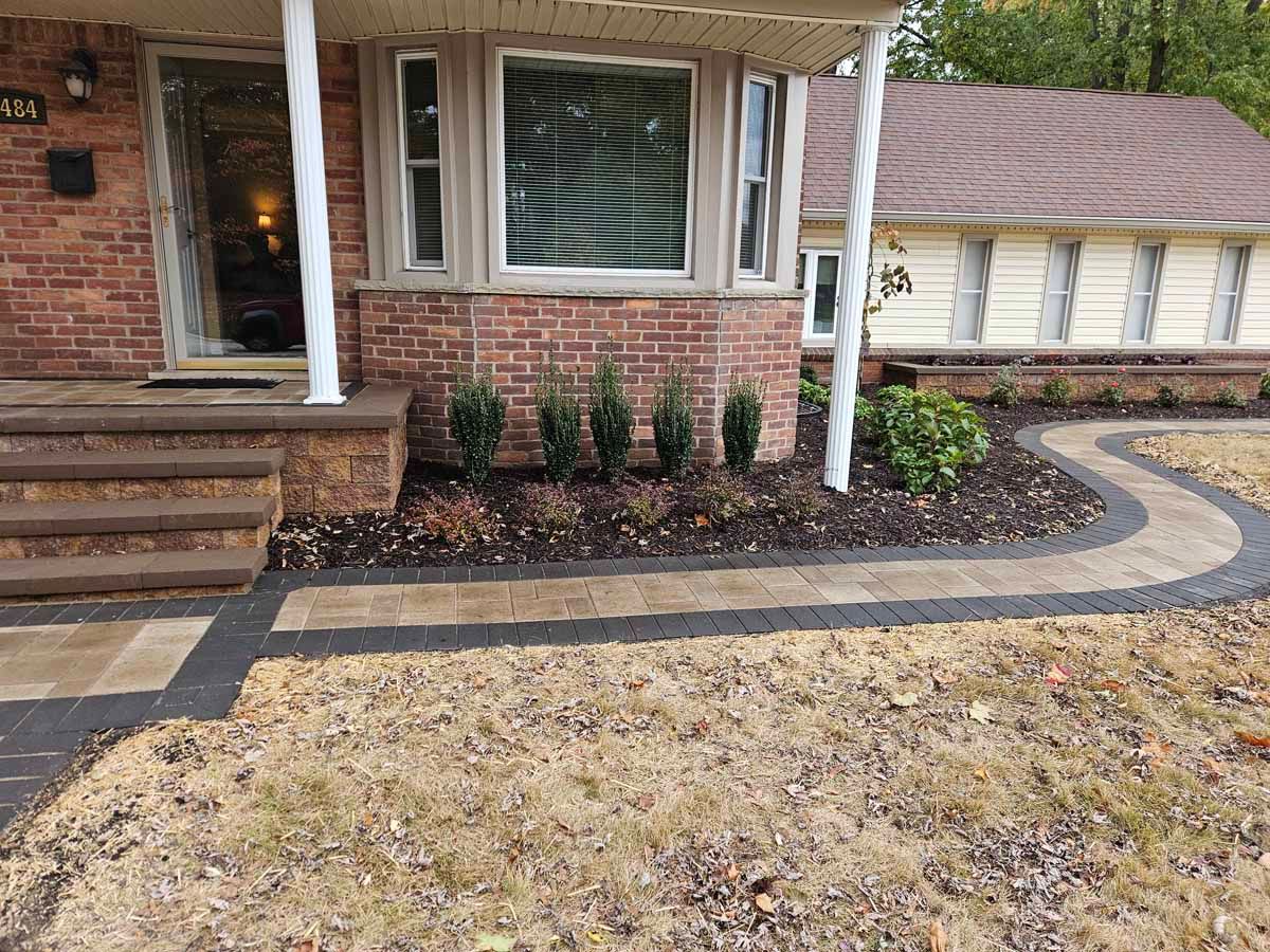 Brick house front porch with steps, windows, flower beds, and a curved paved walkway